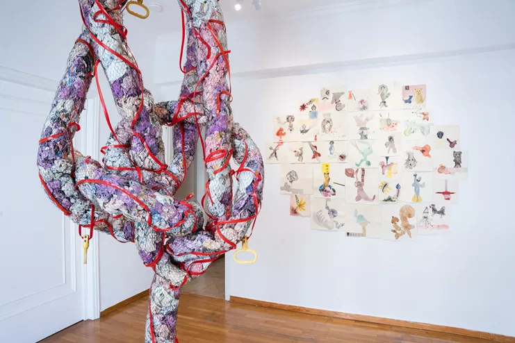 Φωτογραφία εγκατάστασης «Μυθιστορίες ΙΙ». Νάνα Σαχίνη, «who knows what the “and” stands for: story of an acrobat», 2014, 240 x 100 x 80 εκ., papier-mache, χρώμα, συρματόπλεγμα, φωτογραφίες performance, τσιμέντο, πλαστικό καλώδιο (αριστερά). Νάνα Σαχίνη, «the Bible of dreams», 2007 – σε εξέλιξη, διαστάσεις μεταβλητές, μικτή τεχνική σε χειροποίητο χαρτί (δεξιά). Παραχώρηση του καλλιτέχνη και της CITRONNE Gallery